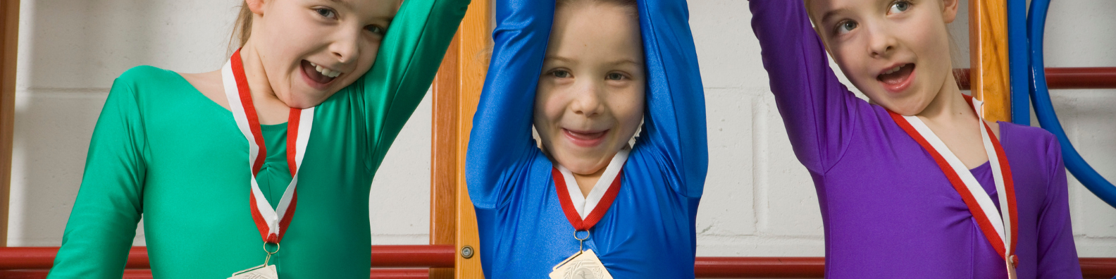 Three young children in leotards with medals around their necks