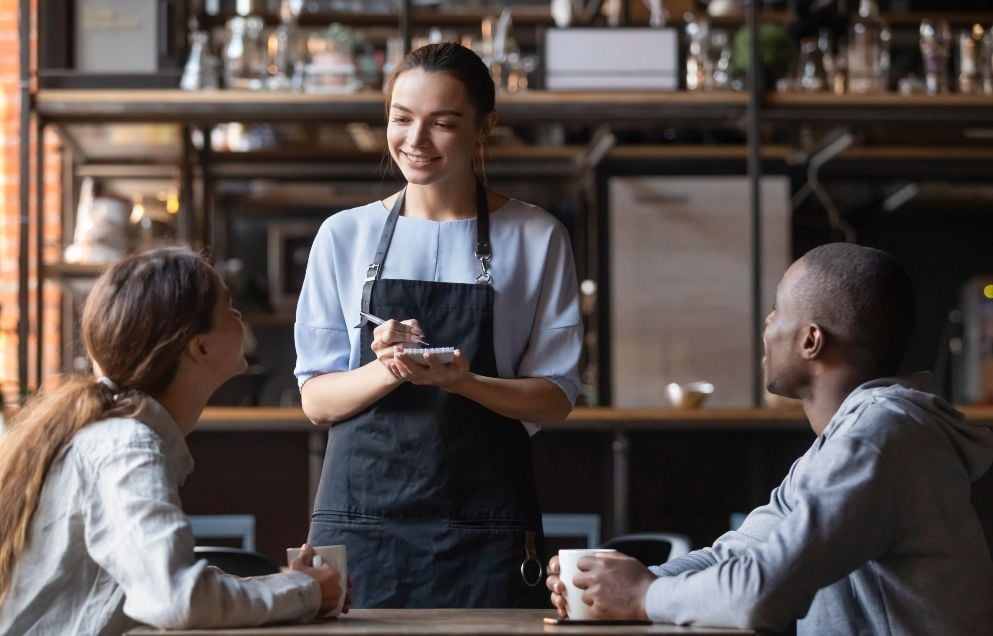 young server talks to two customers in coffee shop setting