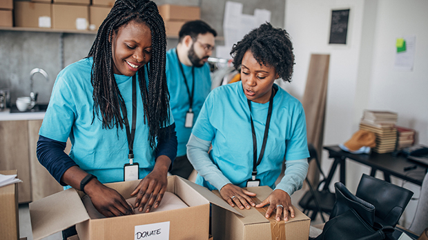 Two people in blue shirts pack donation boxes, while another person works in the background at a community center.