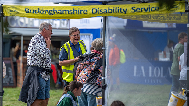 People converse under a "Buckinghamshire Disability Service" tent at an outdoor event; others are nearby.