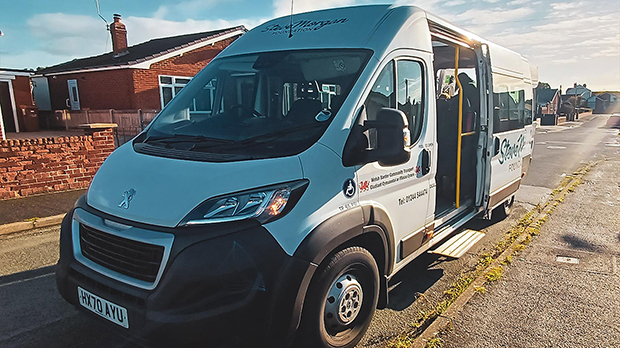 A white Peugeot minibus with side door open is parked on a residential street under clear skies.
