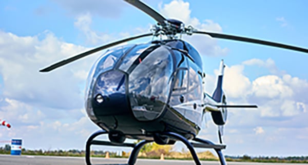 A modern black helicopter is parked on a tarmac under a partly cloudy sky.