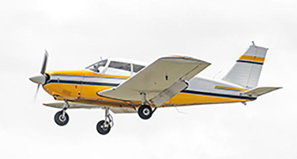 A small yellow and white single-engine propeller airplane is flying against a cloudy sky.