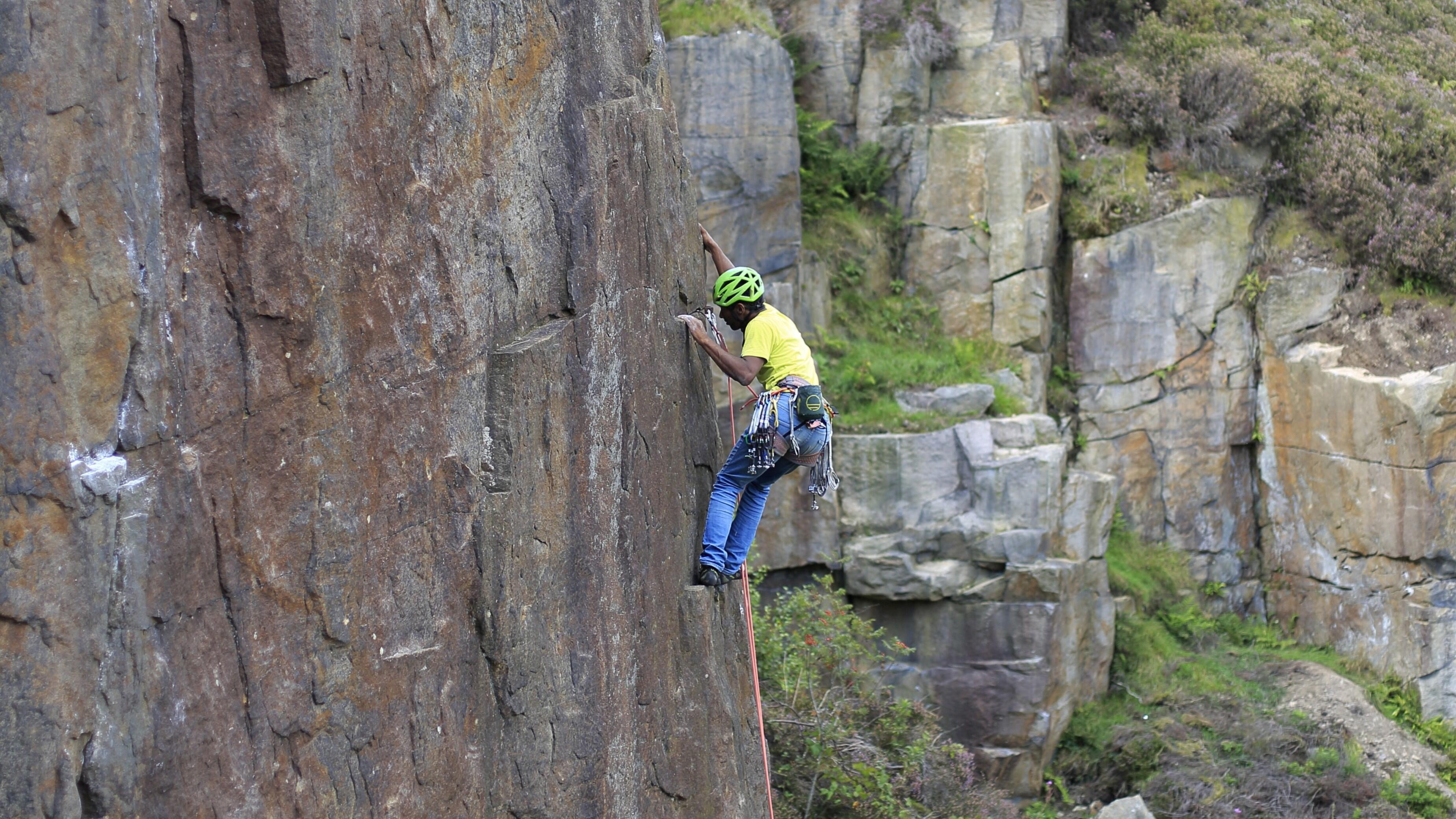 Person climbing up rock with helmet and rope