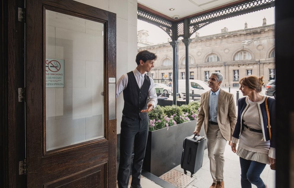 Hotel doorman is welcoming in a mature couple for a weekend break.