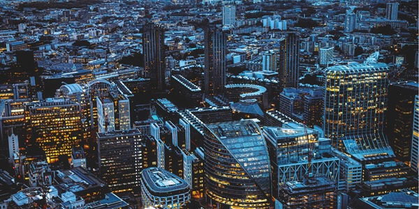 Aerial view of a modern cityscape at dusk, with illuminated office buildings and surrounding urban structures.