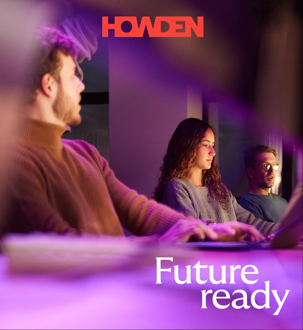 Three people sit at a table with laptops, illuminated by purple light, focused on their screens.
