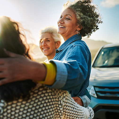 Group of friends in front of a car smiling and enjoying scenery