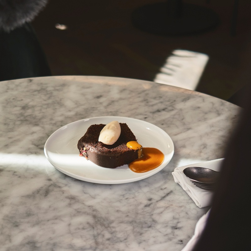 A plated dessert on a marble table under a spotlight in a dimly lit restaurant.