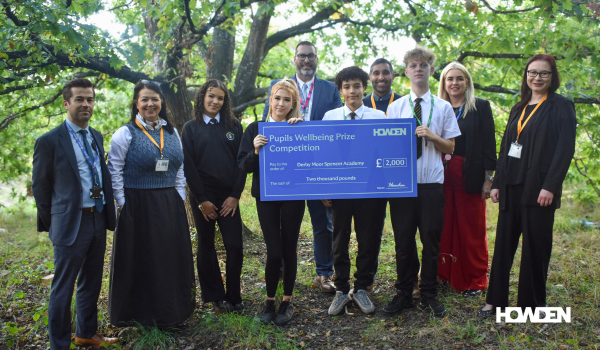 A group of students and adults hold a large £2,000 prize cheque for a pupils' wellbeing competition, outdoors.
