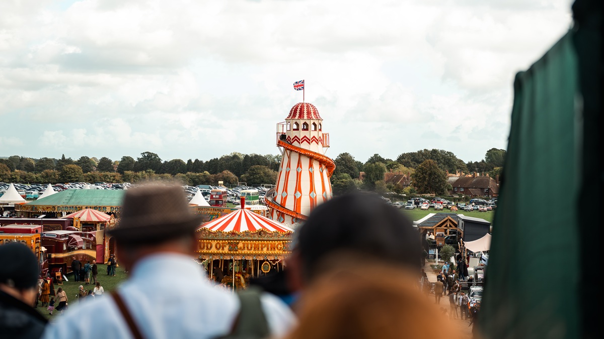 A helter-skelter tower with a British flag stands in a fairground, viewed over a crowd of people.