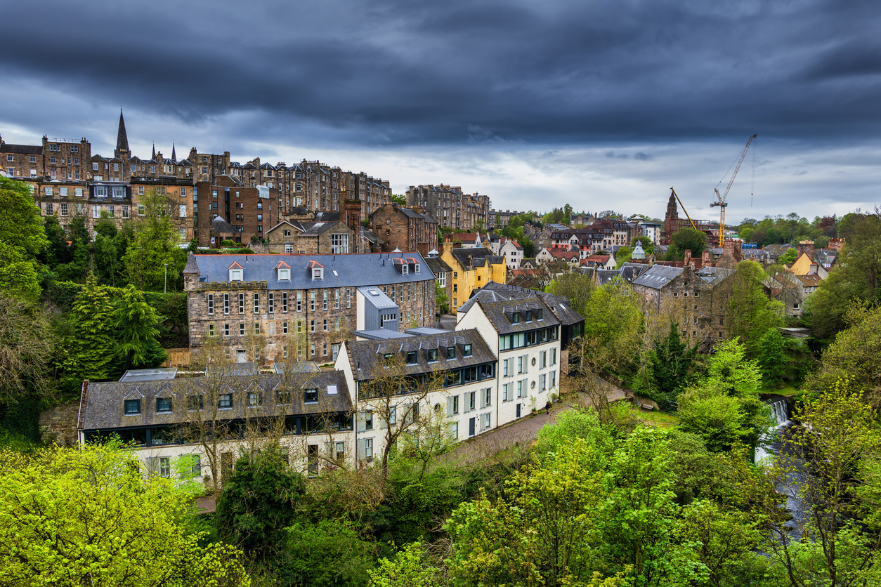 	 Overcast sky above a historic town with stone buildings, lush greenery, and a construction crane in the background.
