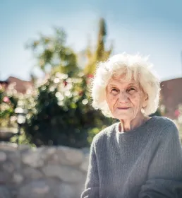 An older lady sits in the sunshine in the garden of a care home