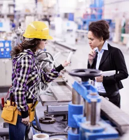 A female inspector speaks with a female construction worker in a factory