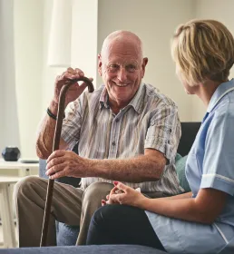An older gentleman smiles as he sits with his carer