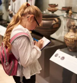 Young girl making notes looking at museum artefacts
