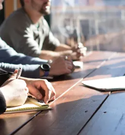 A group of people sitting around a wooden desk in a business meeting
