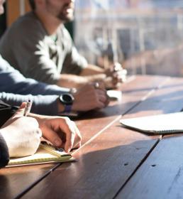 A group of people sitting around a wooden desk in a business meeting