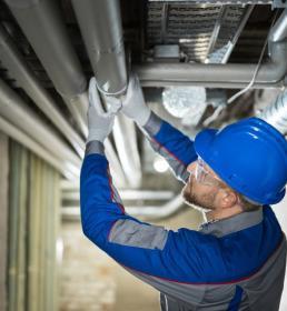 man in hard hat checks overhead pipe for leak