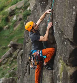 Man climbing up rock with helmet and harness