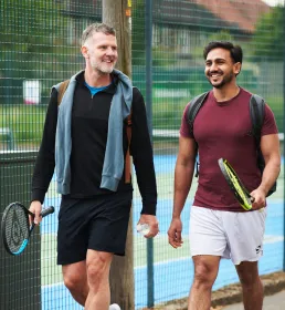 Two men walking past a tennis court