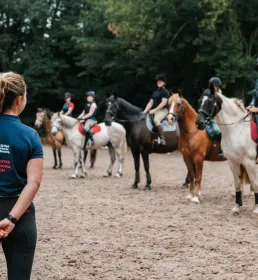 Female coach watching five students on horses in sandschool