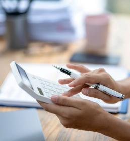 A woman is using a calculator and pen on a desk. She is focused on her work