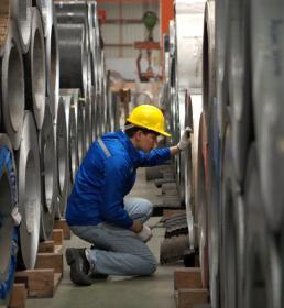 Industrial worker inspecting inside a large metal tube in a factory wearing safety helmet and gloves