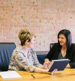 Woman with short blond hair and woman with long dark hair sitting at a desk looking at a screen