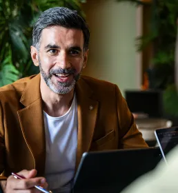 Man in a brown jacket talking with colleague across the table