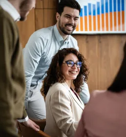 Group of colleagues smiling in a meeting room in front of a chart displayed on screen