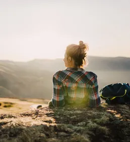 Woman sat on top of mountain, enjoying breath taking view at sunset