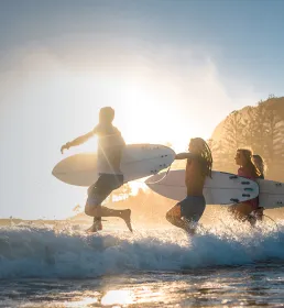Group running out to surf at sunset