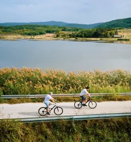 2 cyclists travelling across a lakeside road