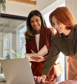 Two colleagues leaning over laptop discussing a project