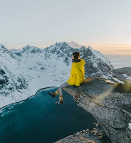 Woman sitting on a cliff edge overlooking snow capped mountains