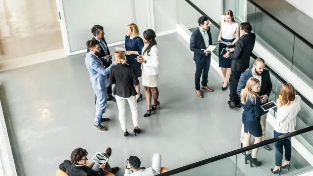 Young professionals stand talking in small groups in the foyer of an office building