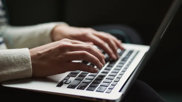 a view of a personns hand typing on a laptop
