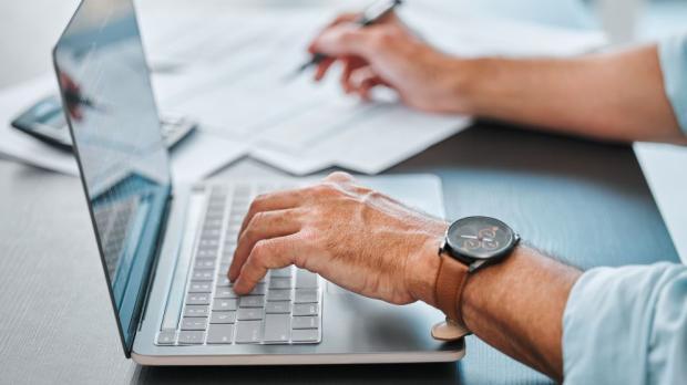 man typing on a laptop and writing on a notepad