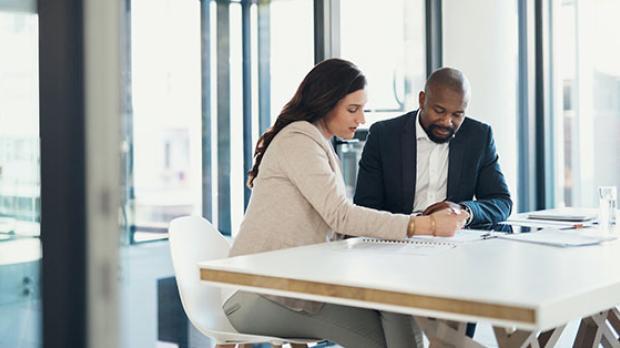 Two people sitting at a table in an office, reviewing documents together.