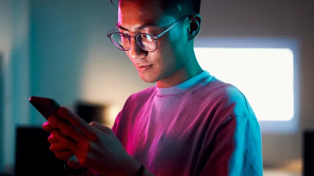 Asian man reviewing his phone in neon lit office