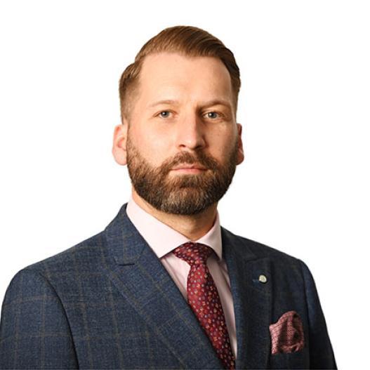 A bearded man wearing a blue suit with shirt and tie 
