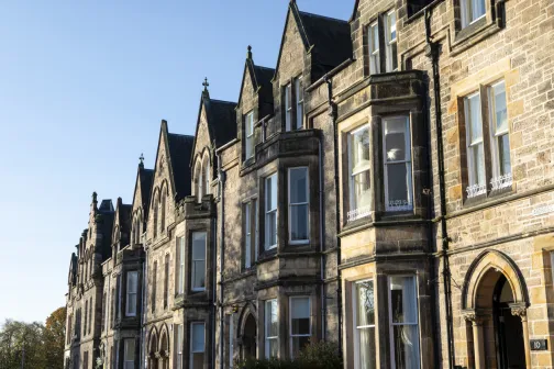 Row of traditional stone townhouses with pointed gables and large windows under a clear blue sky.