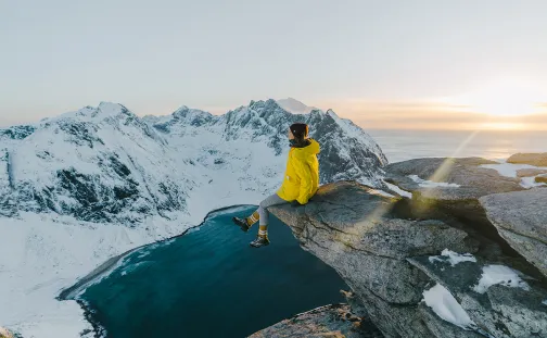 Woman sitting on a cliff edge overlooking snow capped mountains