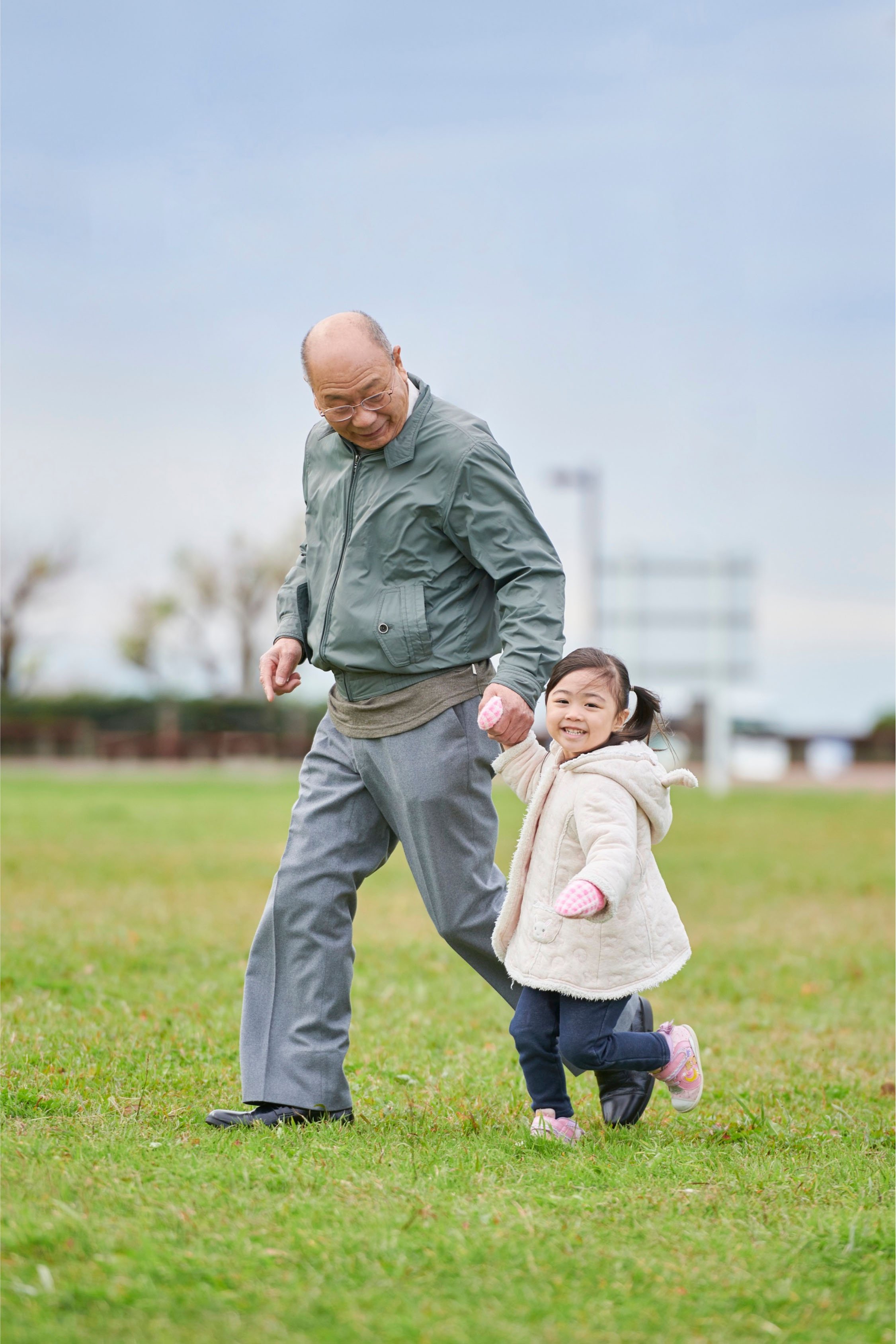 Elderly man holding hands with young girl while walking in a green park, symbolising family care and security in Indonesia