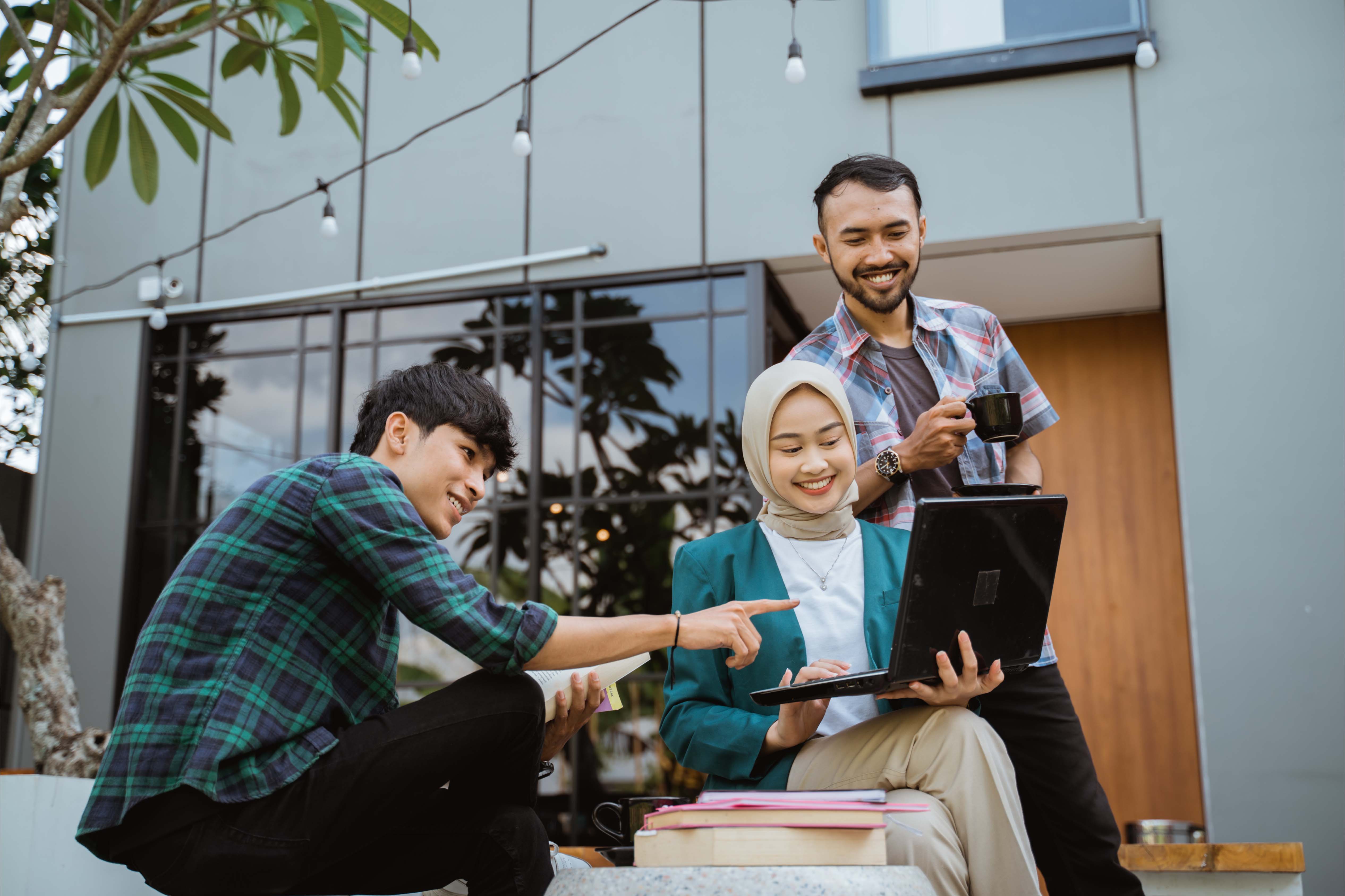 Young Indonesian professionals collaborating outdoors with laptop and coffee