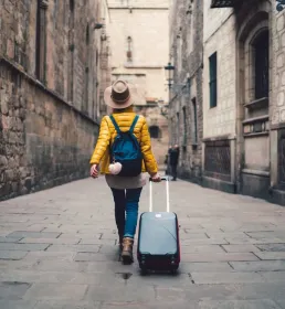 A young woman walks through a Spanish street pulling a suitcase