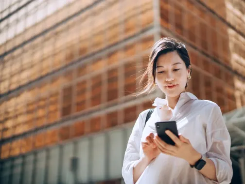 Low angle portrait of young Asian businesswoman checking emails on smartphone outside office building