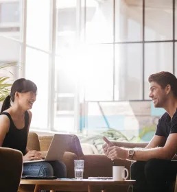 Two young professionals smile together in a modern, bright office