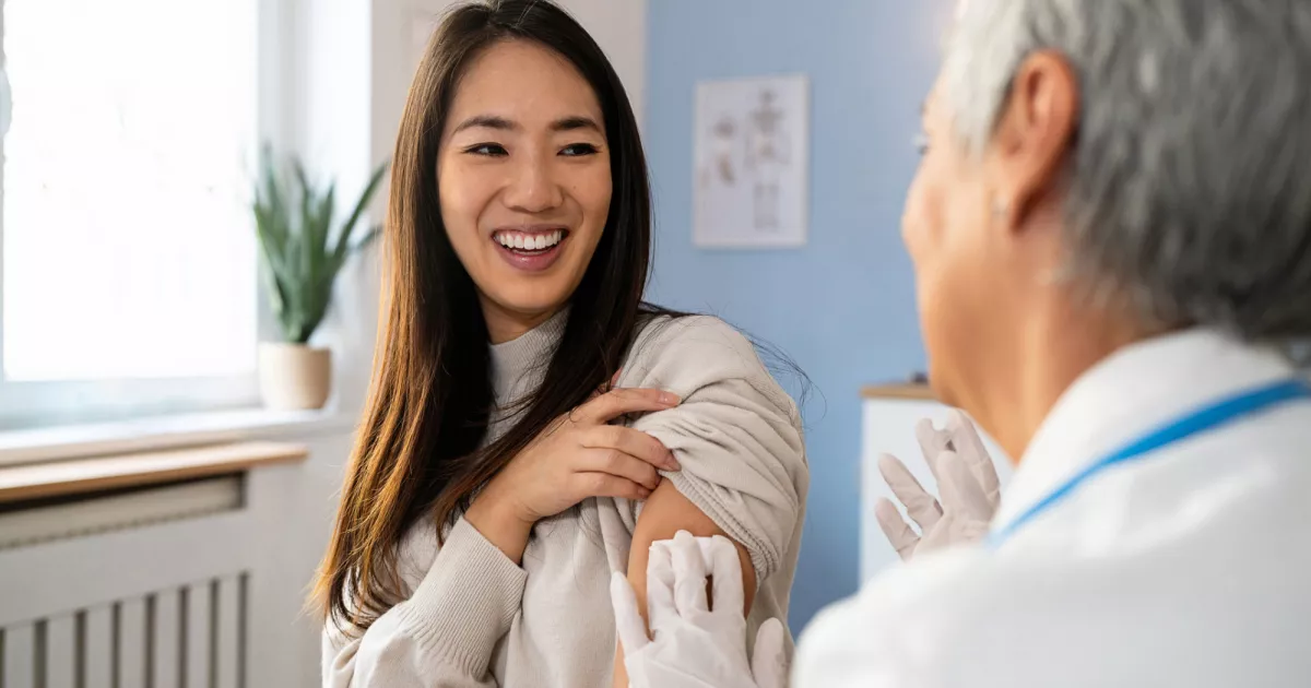Smiling woman at a clinic receiving a vaccination from a medical professional